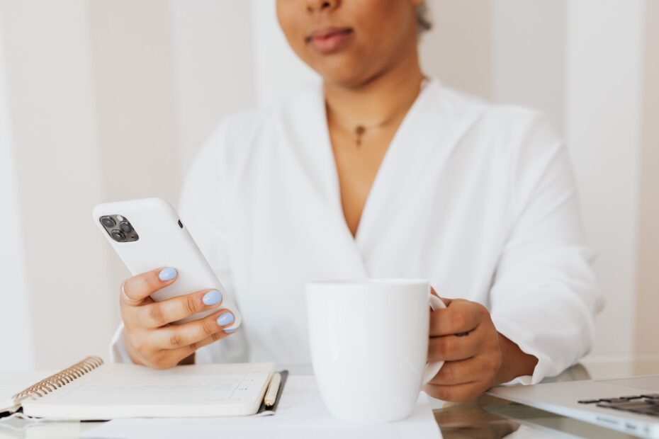 This photo shows someone view a mobile phone and drinking coffee.